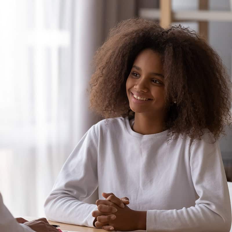 Smiling African American teenage girl sit at table talking with female teacher or tutor at home, happy teenager have casual conversation with woman doctor or specialist. Adult children relationships