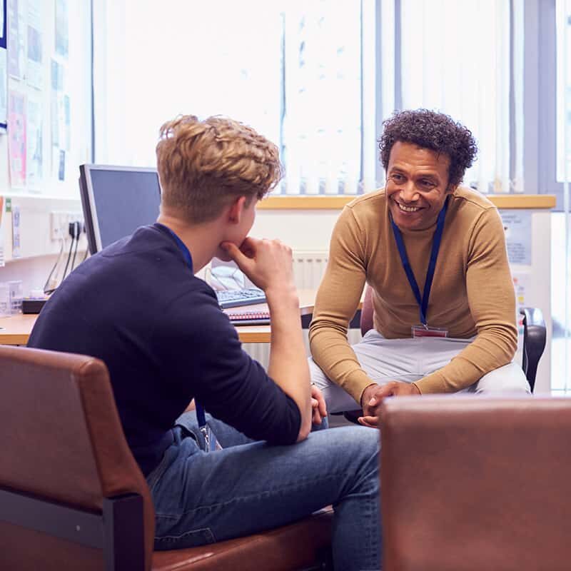 Male College Student Meeting With Campus Counselor Discussing Mental Health Issues